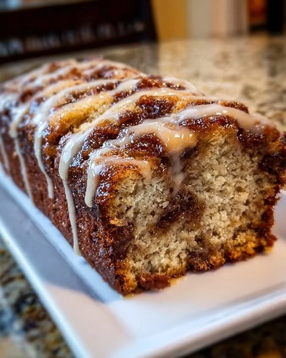 Sliced cinnamon roll banana bread on a wooden table, drizzled with icing.